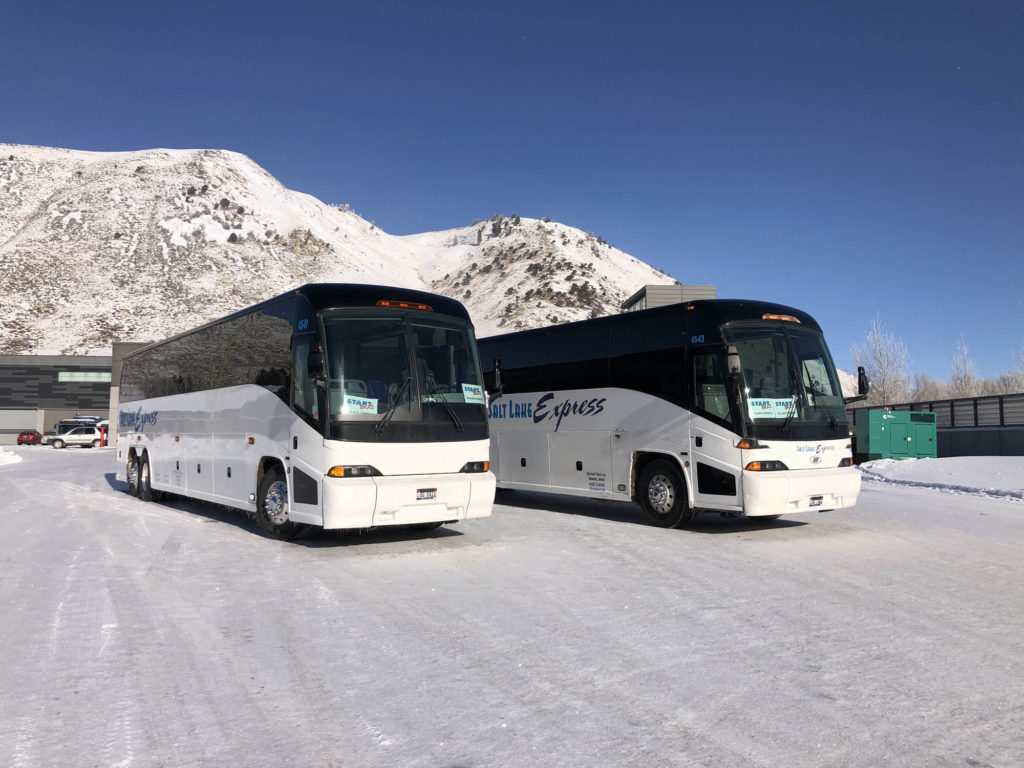 Two chartered buses parked at a ski resort in the snow.